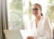 Eine Frau sitzt lachend an ihrem Laptop und freut sich über die gute Online-Bewertung ihrer Immobilie | Immobilienbewertung